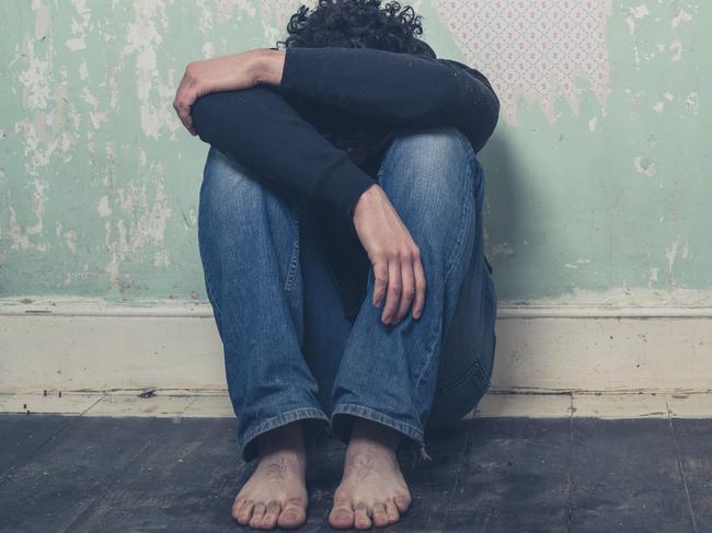 A sad and depressed young man is sitting on the floor in an empty room