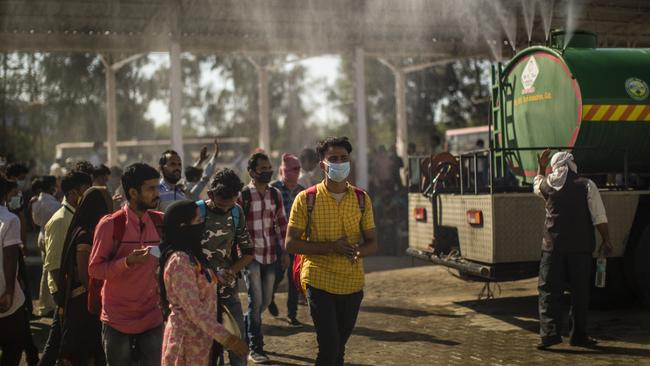 A government vehicle sprays disinfectant on Indian migrant workers waiting to board buses to return to their native villages. Picture: Yawar Nazir/Getty Images