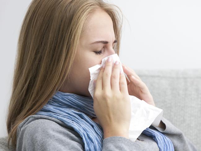 Portrait of a young woman sneezing In to tissue . Source iStock