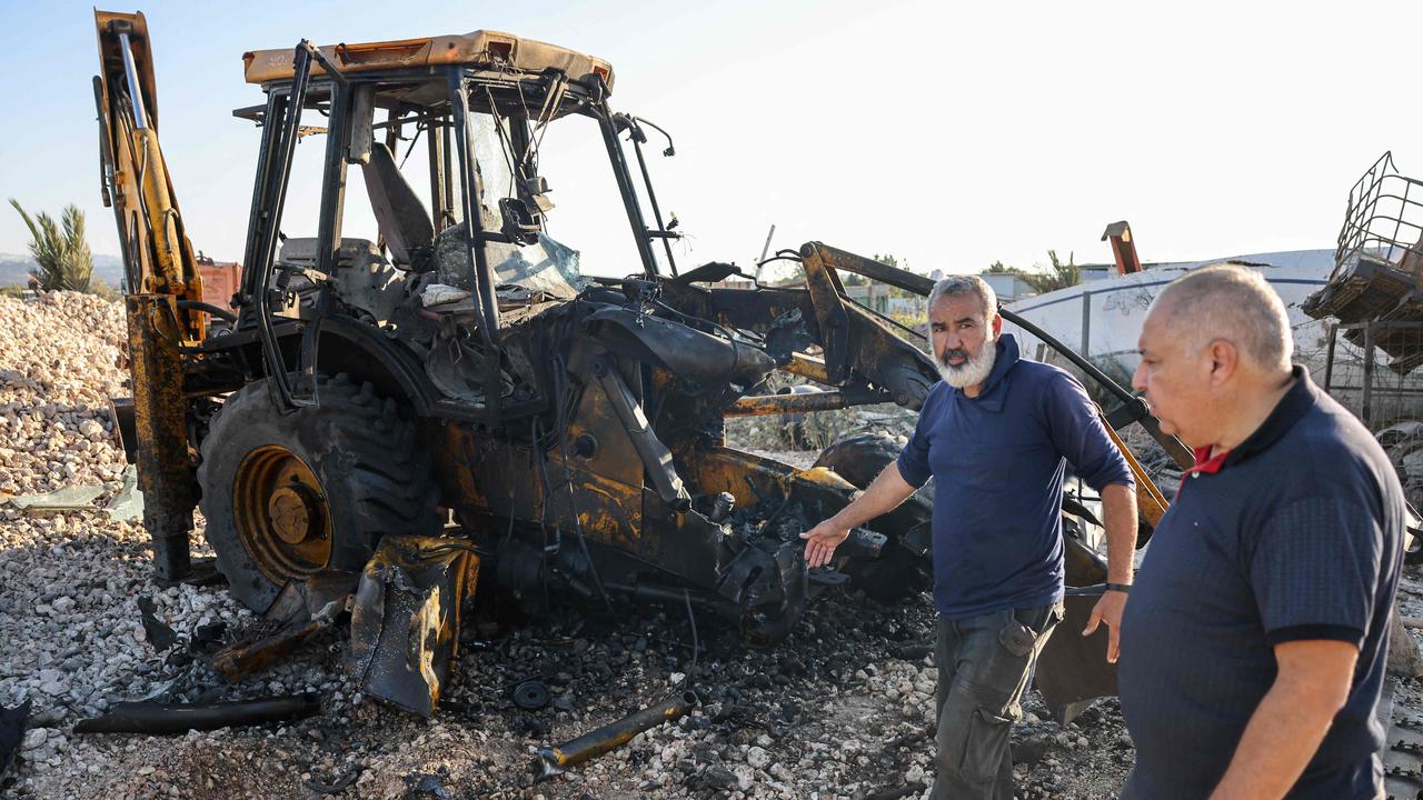 Men walk past a hole in the ground and a burnt tractor after a rocket fired from southern Lebanon hit the town of Kfar Manda. Picture: Ahmad Gharabli/AFP