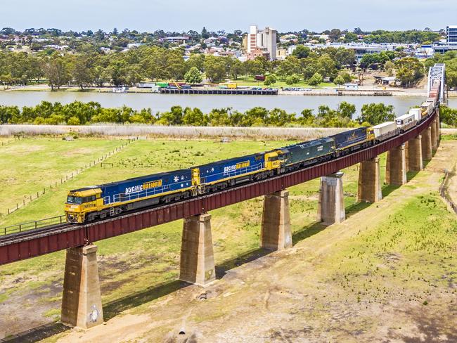 Murray Bridge, Australia - Dec 17, 2021: Aerial view Pacific National intermodal container freight train on viaduct crossing the Murray River floodplain enroute from Perth to Melbourne via Adelaide. The train has four powerful diesel electric locomotives hauling the long train. In the background is the River Murray, the rural town of Murray Bridge and a transport museum on the riverbank.