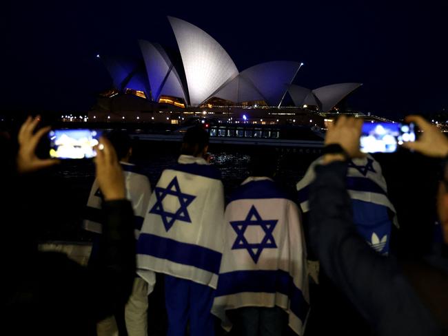 People with Israeli flags watch the Opera House while it is illuminated in blue to show solidarity with Israel in Sydney. Picture: David Gray/AFP