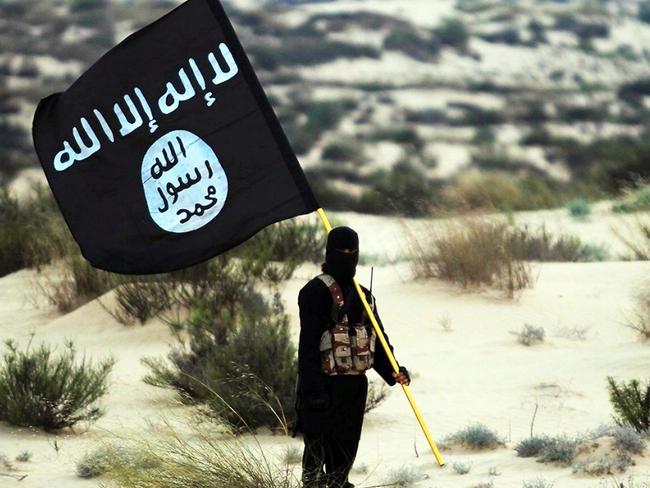 Islamic State/Iraq/Syria: A masked Islamic State soldier poses holding the ISIL banner somewhere in the deserts of Iraq or Syria. ISIL publicity image, 2015. (Photo by: Pictures from History/Universal Images Group via Getty Images)