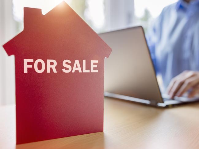 Man using laptop searching for real estate or new house on the internet with for sale sign on red house