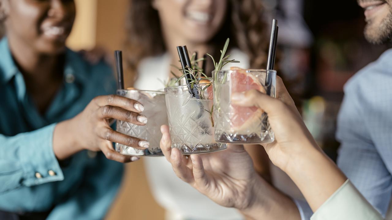 People with alcohol drinks clinking glasses in a restaurant having fun together, laughing, drinking cocktails. Party, celebration, nightlife and people concept - smiling friends clinking glasses