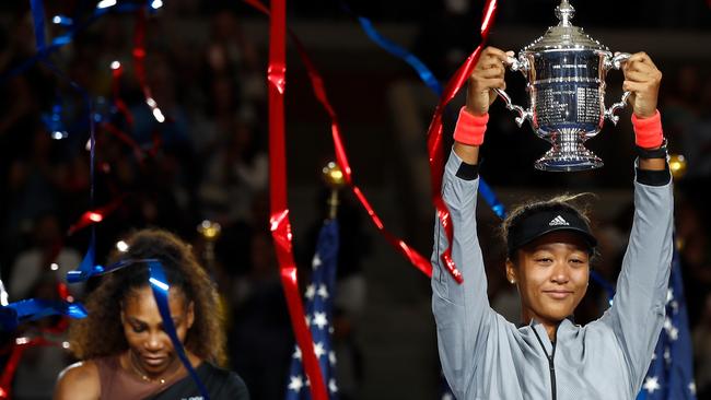 Naomi Osaka with the championship trophy with Serena Williams in the background. Picture: Julian Finney/Getty Images