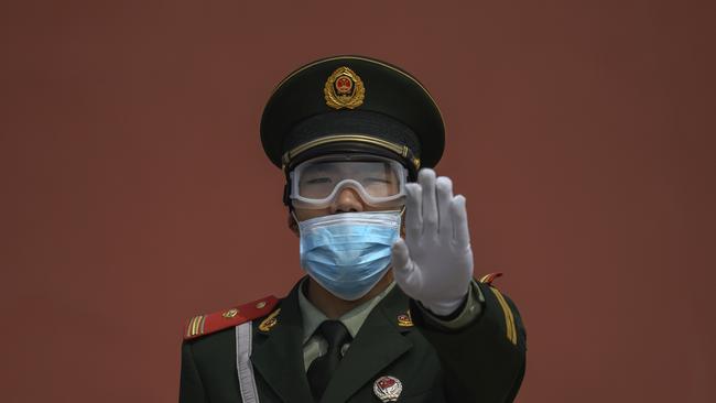 A Chinese paramilitary police officer gestures as he wears a protective mask while standing guard at the entrance to the Forbidden City.