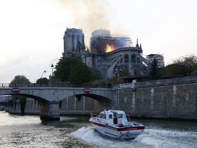 A speedboat travels down the river Seine as flames and smoke rise from Notre Dame cathedral as it burns in Paris, Monday, April 15, 2019. (AP Photo/Thibault Camus)