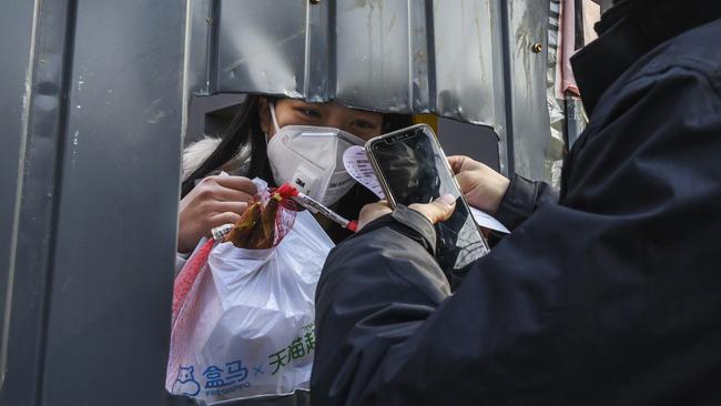 A Chinese woman wears a protective mask as she accepts a package from a courier through a cutout hole in a makeshift barricade wall. Picture: Kevin Frayer/Getty Images.