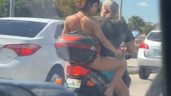 Woman shaves legs on back of moped