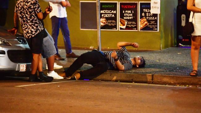 GONE! A young New Year's Eve reveller lies prone on Mitchell St as his mates look on in the early hours of New Year's day