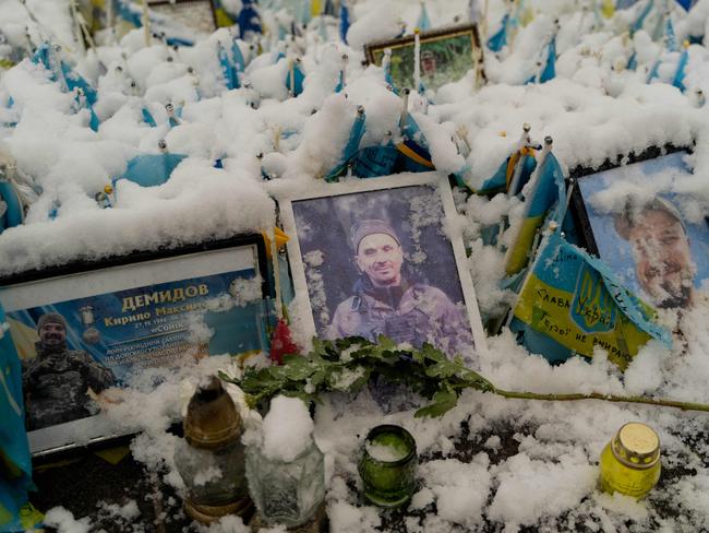 TOPSHOT - Portraits of Ukrainian military members covered in snow are seen at the makeshift memorial to Ukrainian and foreign fighters, at the Independence Square in downtown Kyiv, on November 21, 2024, amid the Russian invasion of Ukraine. (Photo by Tetiana DZHAFAROVA / AFP)