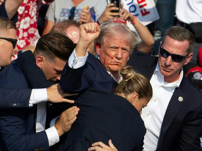 TOPSHOT - Republican candidate Donald Trump is seen with blood on his face surrounded by secret service agents as he is taken off the stage at a campaign event at Butler Farm Show Inc. in Butler, Pennsylvania, July 13, 2024. Donald Trump was hit in the ear in an apparent assassination attempt by a gunman at a campaign rally on Saturday, in a chaotic and shocking incident that will fuel fears of instability ahead of the 2024 US presidential election. The 78-year-old former president was rushed off stage with blood smeared across his face after the shooting in Butler, Pennsylvania, while the gunman and a bystander were killed and two spectators critically injured. (Photo by Rebecca DROKE / AFP)