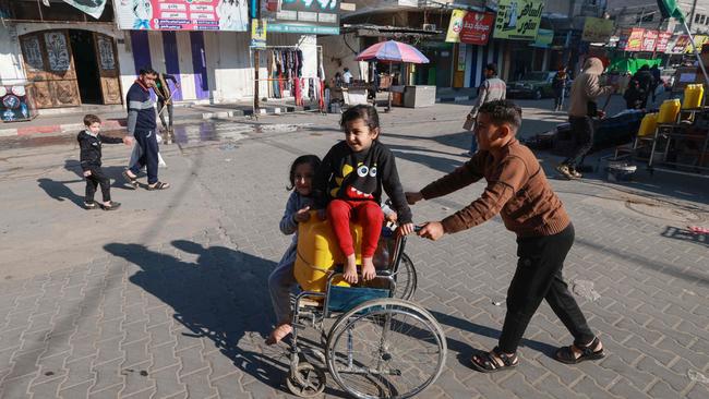 A Palestinian boy pushes a girl sitting on a wheelchair with a water canister as displaced families struggle to get their basic survival needs in the Rafah refugee camp. Picture: AFP