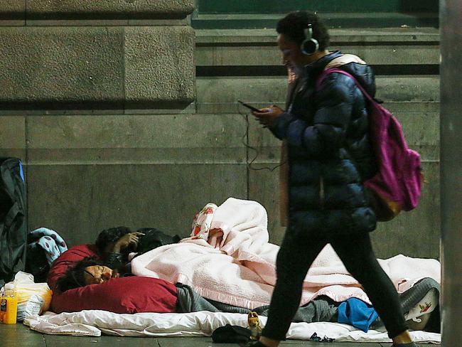 A man sleeps on the path in Flinders Street as a pedestrian passes by. Picture: Ian Currie