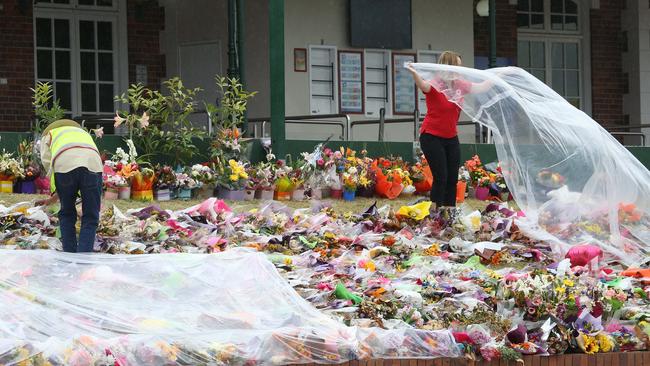 Red Cross volunteers cover the floral tributes with plastic to protect them from rain. Picture: Scott Fletcher