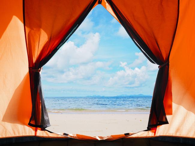 Looking through opening door of orange tent camping to summer beach background.