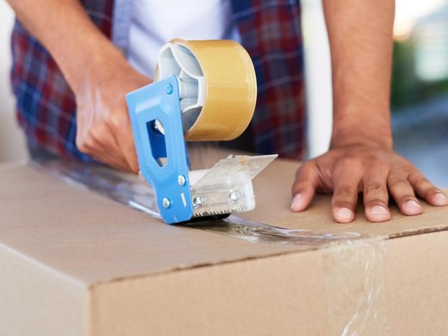 Shot of an unidentifiable man using a tape dispenser to close a box while moving house