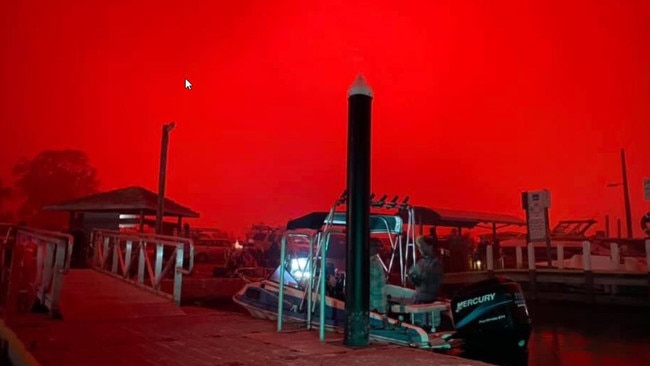 The skies above Mallacoota wharf were red yesterday morning as residents and holiday-makers fled to the foreshore. Picture: Bradley Deacon