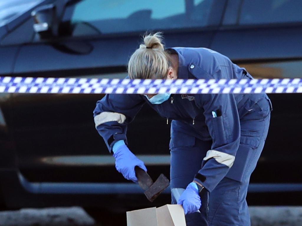 A police officer picks up a hatchet at the scene. Picture: David Crosling