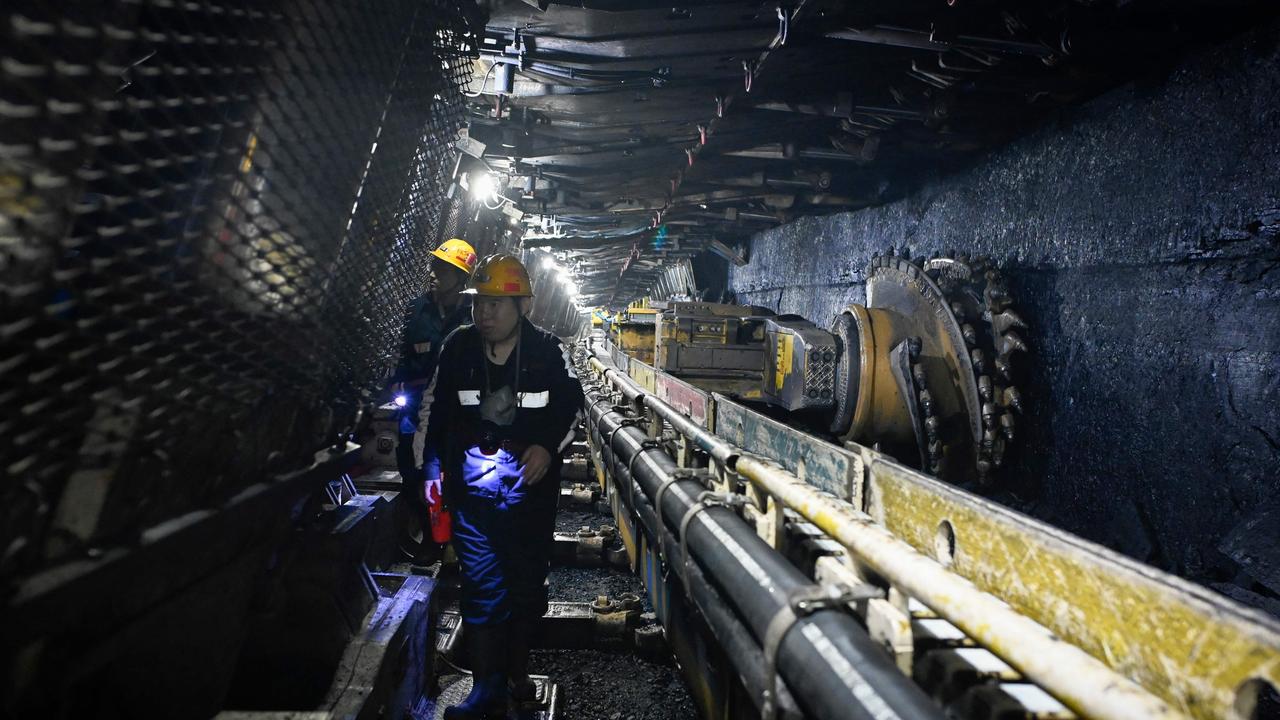 Two miners walk past a shearer while underground in a Hongliulin coal mine in China. (Photo by WANG Zhao / AFP)