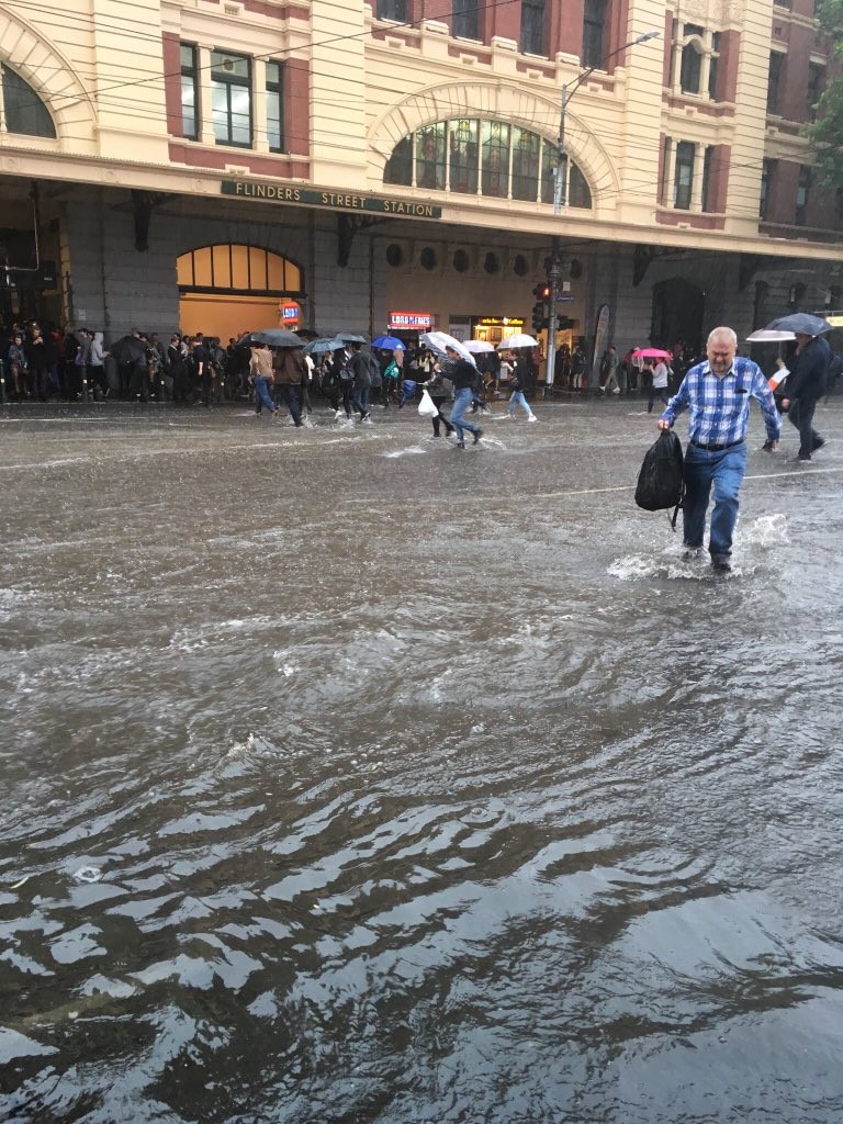 Pedestrians cross a flooded Flinders St. Picture: Twitter/@joannamuses