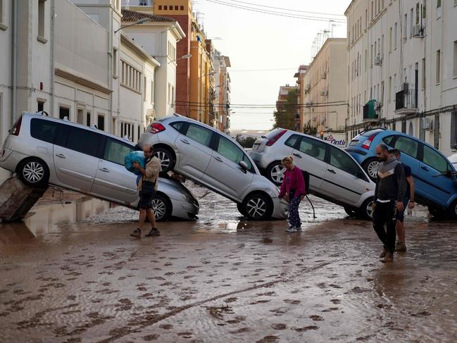 Residents walk past piled up cars following deadly floods in Valencia’s De La Torre neighbourhood. Picture: AFP