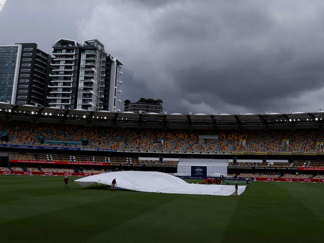 Groundsmen cover the pitch as storm clouds gather over The Gabba on the final day of the third Test match between Australia and India in Brisbane on December 18, 2024. (Photo by David GRAY / AFP) / âIMAGE RESTRICTED TO EDITORIAL USE - STRICTLY NO COMMERCIAL USE --