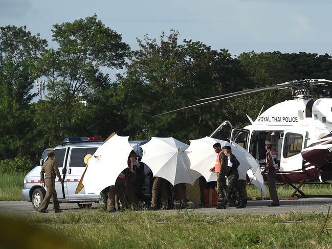 Thai police and military personnel use umbrellas to shield a helicopter evacuation at a military air base in Chiang rai as operations continue. Picture: AFP