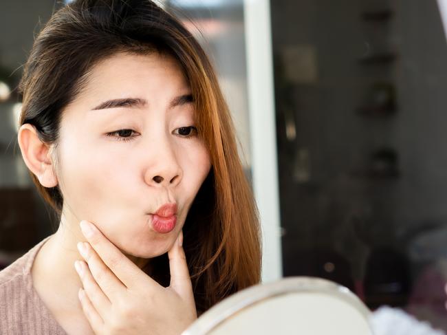 Asian woman doing face yoga , exercises for anti-aging, slimming face in front of mirror