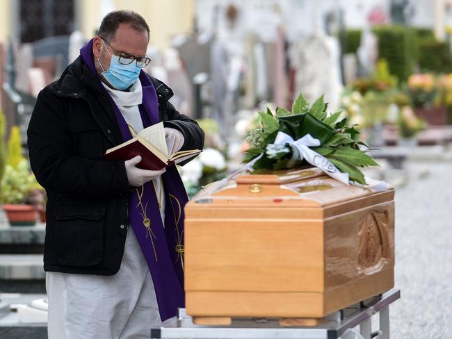 A priest wearing a face mask checks a book of funeral rites as he gives the last blessing tduring a funeral ceremony outside the cemetery of Bolgare, Lombardy. Picture: AFP