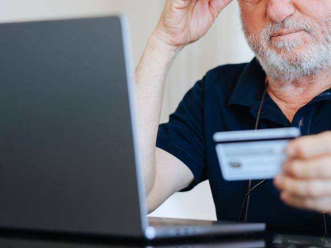 Upset senior elderly man holding credit card by laptop having trouble worry finance safety data or online payment security. Bank client concerned about problem with credit card, financial fraud threat; confusion generic