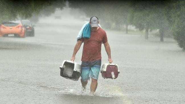 Peter Sharpe carries a pair of cats to safety in Carmody Street, Rosslea, as heavy rain lashes Townsville. Picture: Evan Morgan