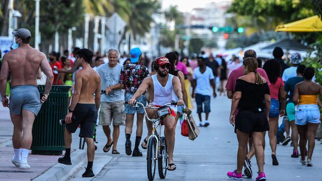 A man rides a bicycle as people walk on Ocean Drive in Miami Beach, Florida on June 26.