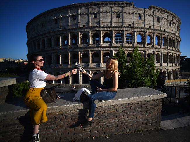 Young women clink bottles of beer as they share an aperitif drink by the Colosseum monument in Rome. Picture: AFP