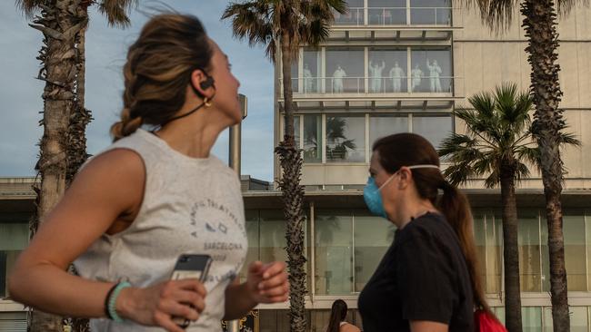 Medical staffers in Personal Protective Equipment (PPE) wave to people exercising outdoors at Hospital del Mar in Barcelona. Picture: Getty Images