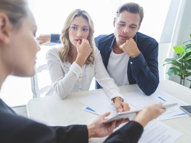 Real estate agent with couple looking through documents. The agent is holding a digital tablet showing it to the clients. Couple are casually dressed. first home buyer generic sad, stressed