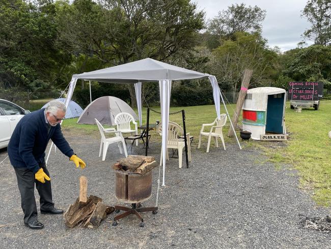 Self-proclaimed Dr Wayne Miller adds another log to the pile at his pop up protest. Picture: NewsLocal