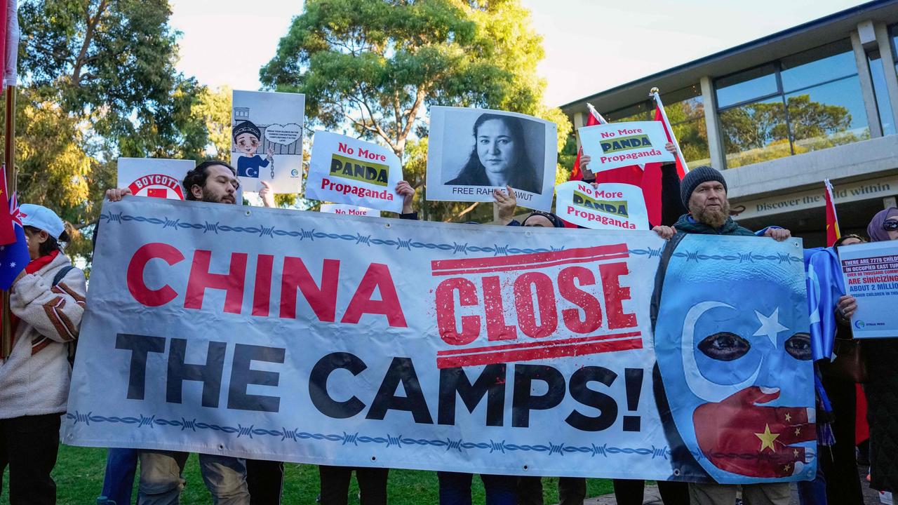 Uyghur and counter-China demonstrators hold a banner and placards as they await the arrival of China's Premier Li Qiang.