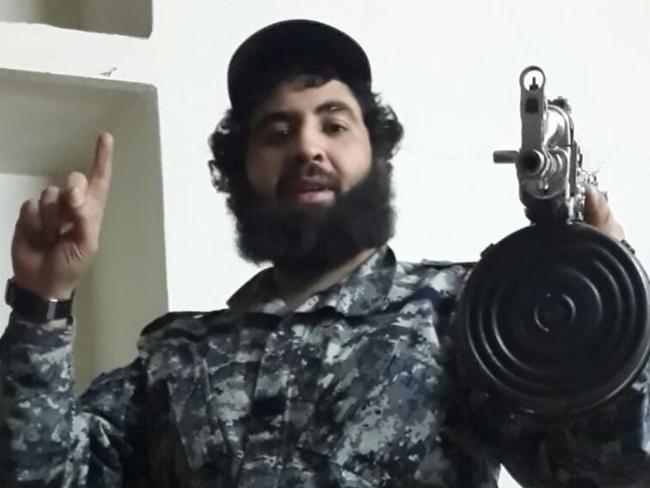 Clad in military fatigues, Sydney man Ahmed Merhi holds a large assault rifle while posing for a photo.