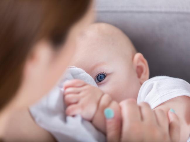 Cute baby looks up at her mother while breastfeeding. One of the baby's blue eyes is looking at her mom.