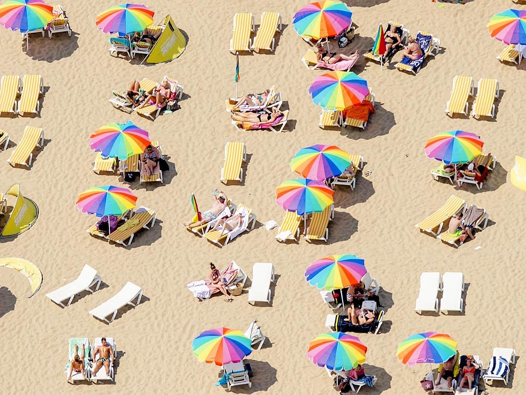 An aerial view shows sunbathers sitting under colorful umbrellas on the beach in Scheveningen, the Netherlands, on July 1, 2015, on a warm summer day. Picture: AFP