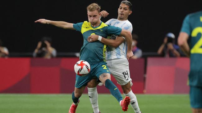 Australia's defender Nathaniel Atkinson (C) controls ball next to Argentina's defender Facundo Medina during the Tokyo 2020 Olympic Games men's group C first round football match between Argentina and Australia at the Sapporo Dome in Sapporo on July 22, 2021. (Photo by ASANO IKKO / AFP)