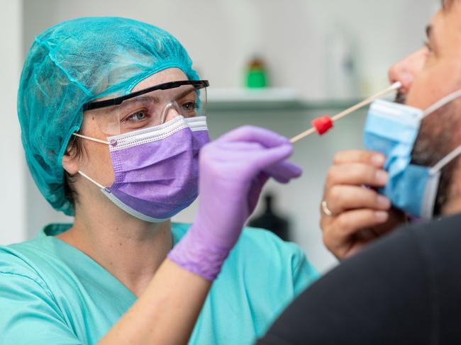 Female doctor in protective workwear taking nose swab test from middle aged man wearing protective face mask, Covid-19 pandemic outbreak