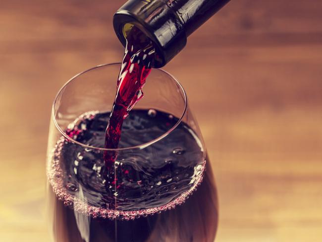 Pouring red wine into the glass against wooden background