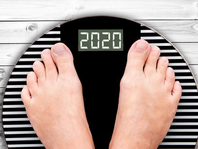 2020 feet on a weight scale on white planks, new year and holiday food nutrition and diet concept