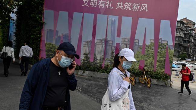 People wearing faces masks as a precaution against COVID-19 walk past a billboard promoting their city in Wuhan, China, where coronavirus made its first known appearance. Picture: AFP