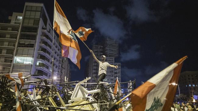 An anti-government protester waves a Lebanese flag as he stands on top of a pile of broken tents in Martyrs' Square in Beirut. Picture: Getty Images.