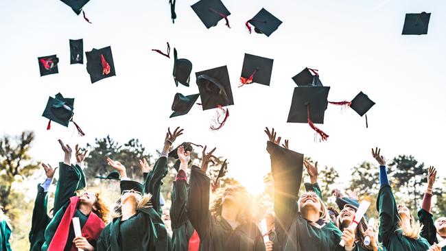 Generic stock photo showing a large group of happy college students celebrating their graduation day outdoors while throwing their caps up in the air.