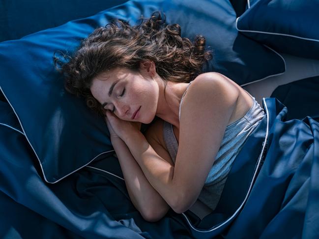 Top view of young beautiful woman dreaming in bed and relaxing at night. High angle view of woman with closed eyes sleeping well at home in the dark. Beautiful girl sleeping peacefully under blue blanket in her bedroom at late in night. Photo: iStock